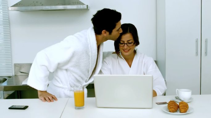 一个男人在女朋友用笔记本电脑吃早餐时亲吻她