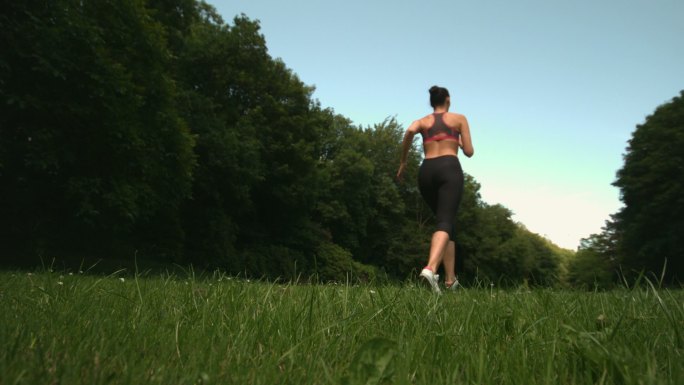 低角度的运动妇女在草地上跑慢的动作