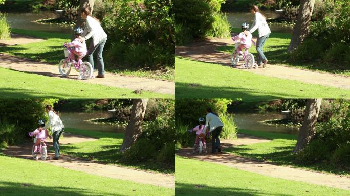 妈妈教女儿骑自行车在公园特写