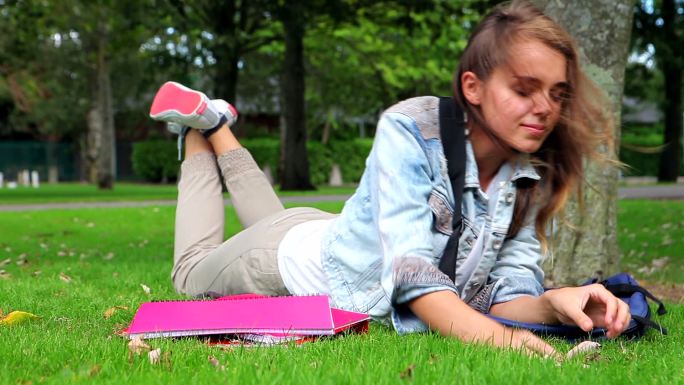 学生趴在校园的草地上看手机特写