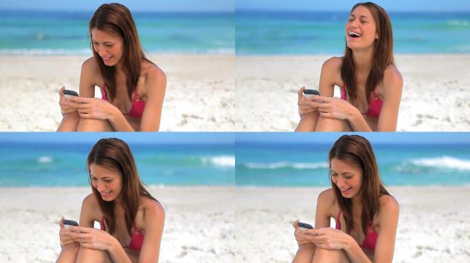 快乐的褐发女人坐在沙滩上玩手机