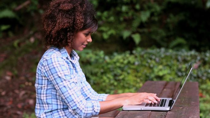 华丽的内容，褐发女人坐在野餐桌上使用笔记本电脑在一个公园