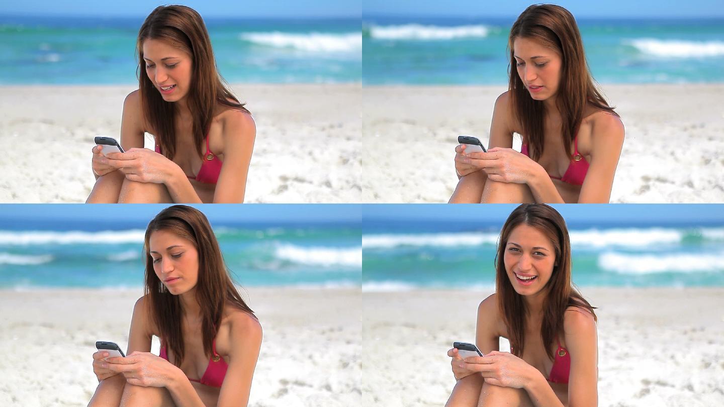 微笑的黑发女子坐在沙滩上发短信