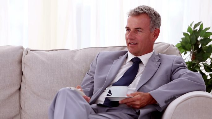 男人拿着遥控器和茶坐在沙发上看电视特写
