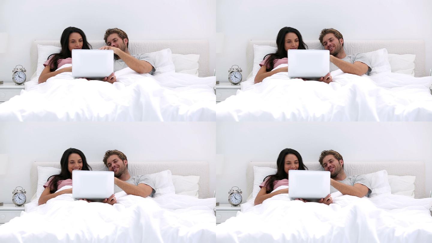 一对夫妇趴在床上看电脑特写