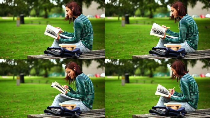 漂亮的学生坐在长凳上看书，在大学里听着音乐