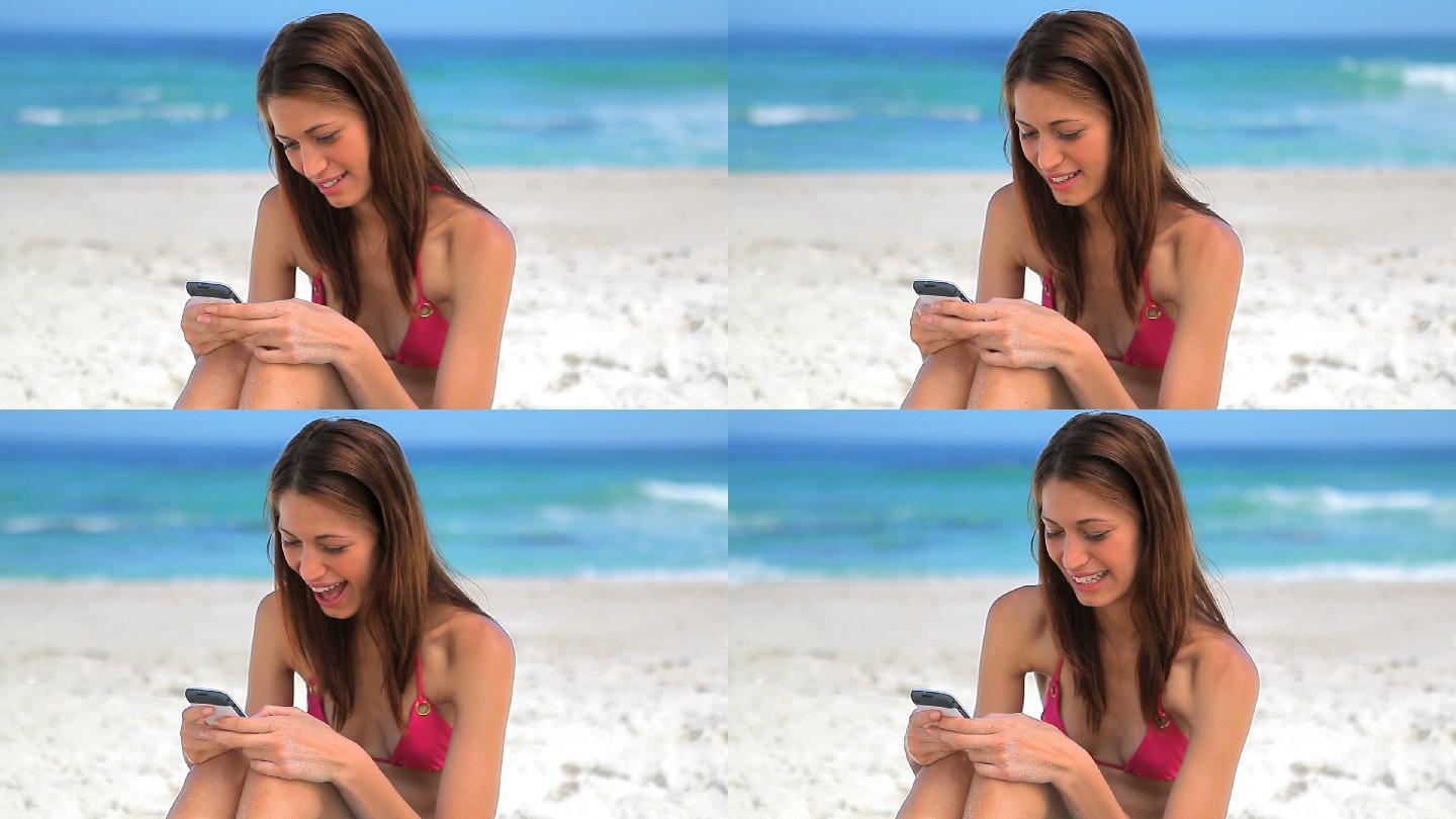 女人坐在沙滩上玩手机特写
