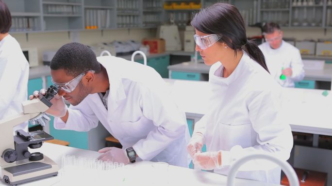 穿着实验服在实验室里透过显微镜看的学生
