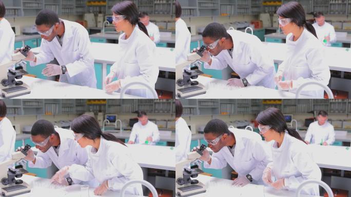 穿着实验服在实验室里透过显微镜看的学生