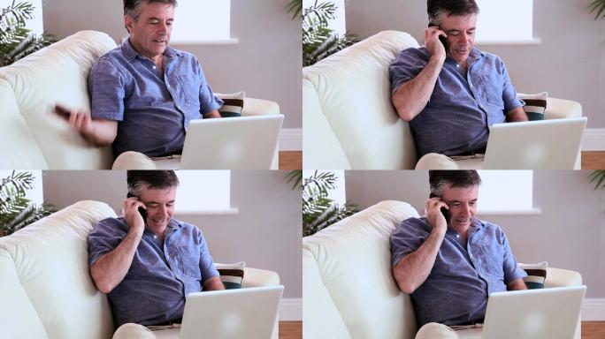 一个成熟的男人坐在沙发上，在客厅里用笔记本电脑接电话