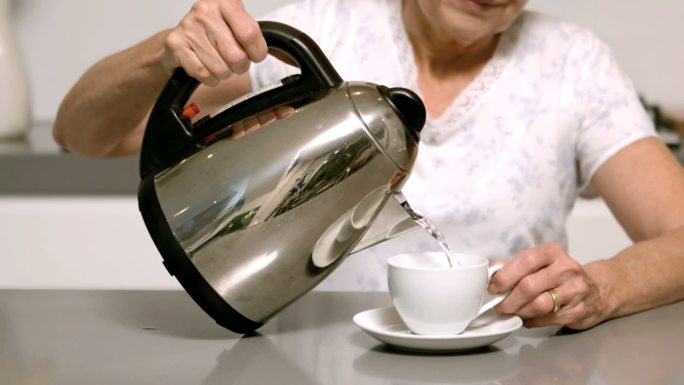 老妇人将沸水从水壶倒入杯中特写