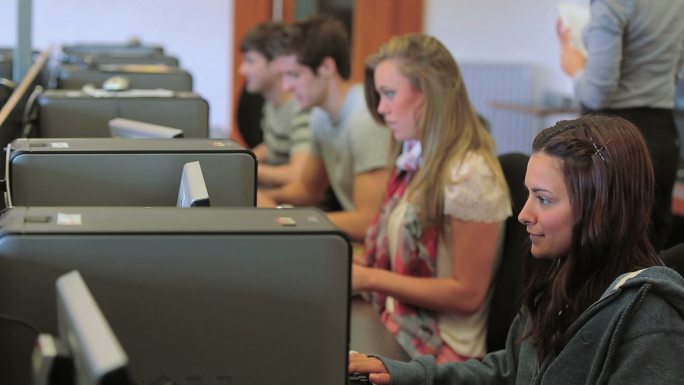 在大学计算机课上，学生集中精力在计算机上，而老师在后面
