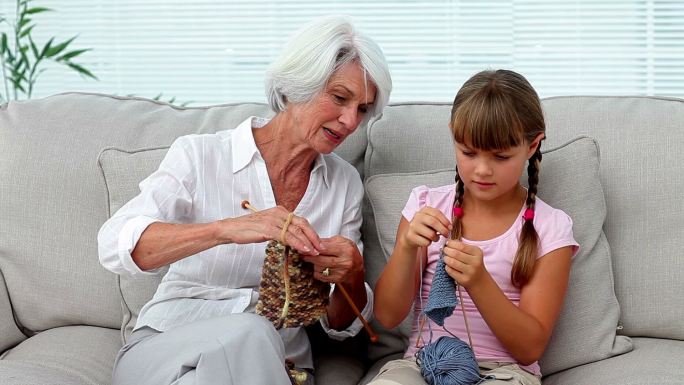 奶奶在家里的沙发上教她的孙女如何织毛衣