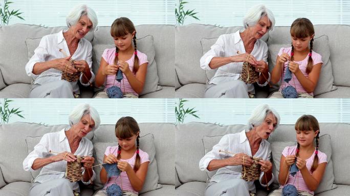 奶奶在家里的沙发上教她的孙女如何织毛衣