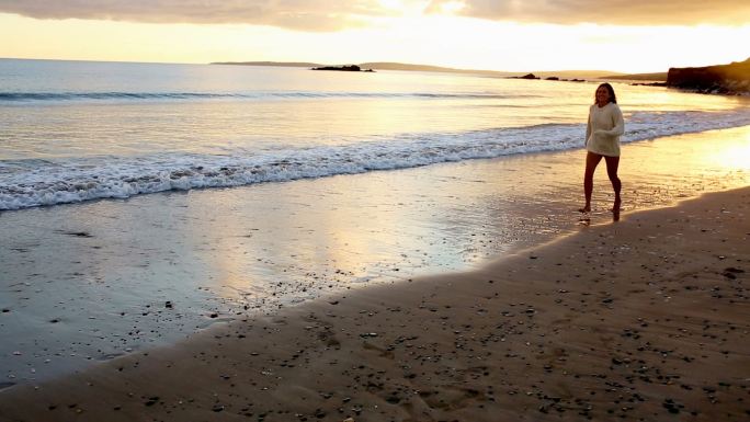 日落时分，海滩上的女人在水里蹦蹦跳跳