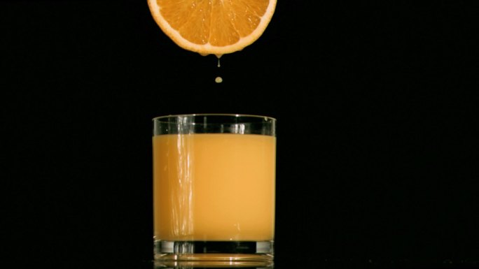 橙汁从橙子中滴落到杯子里特写
