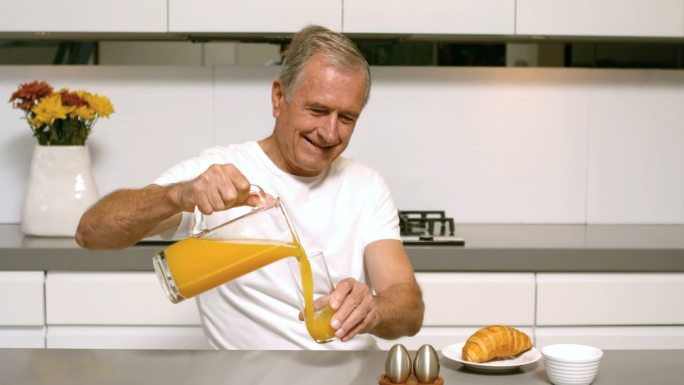 一名退休男子在厨房里慢镜头地为早餐倒橙汁