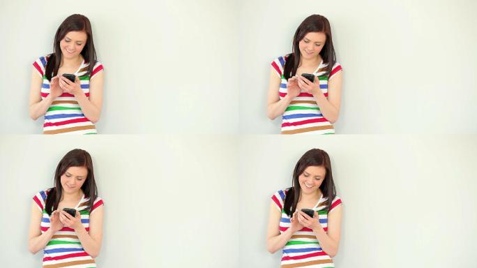 一个快乐的年轻女子，靠在白墙上用手机发短信