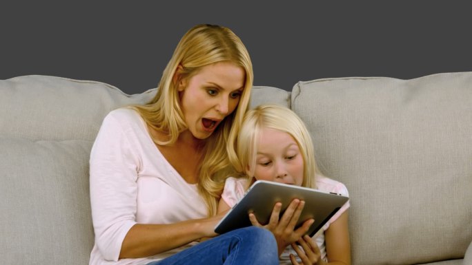 母亲和女儿坐在沙发上看平板电脑特写