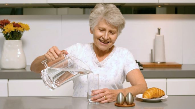 一位退休妇女在厨房里慢动作地倒着一杯早餐水