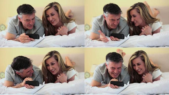 一对夫妇趴在床上看手机特写