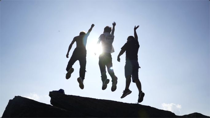 三个年轻人登山逆光欢呼追梦人登山跳跃庆祝