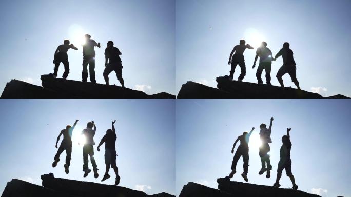 三个年轻人登山逆光欢呼追梦人登山跳跃庆祝