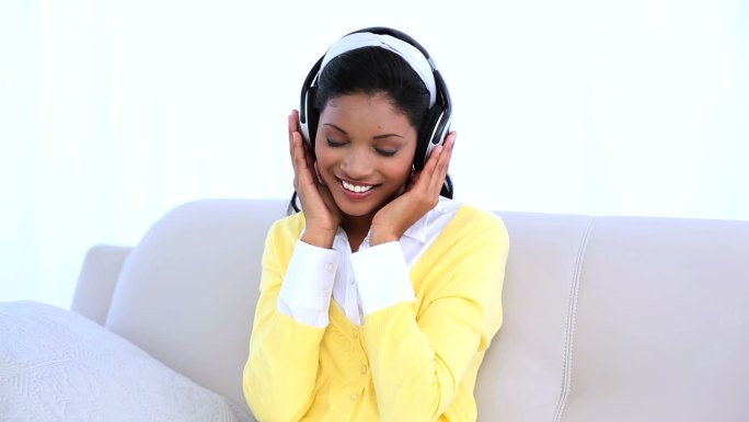 女人戴着耳机坐在家里的沙发上听音乐