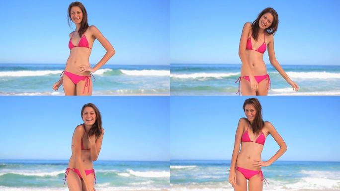 女人穿着粉色比基尼站在沙滩上微笑特写