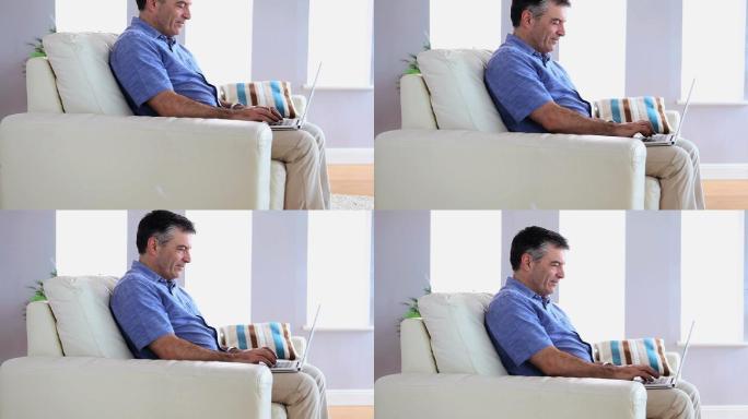 一个成熟的男人在客厅的沙发上使用他的笔记本电脑