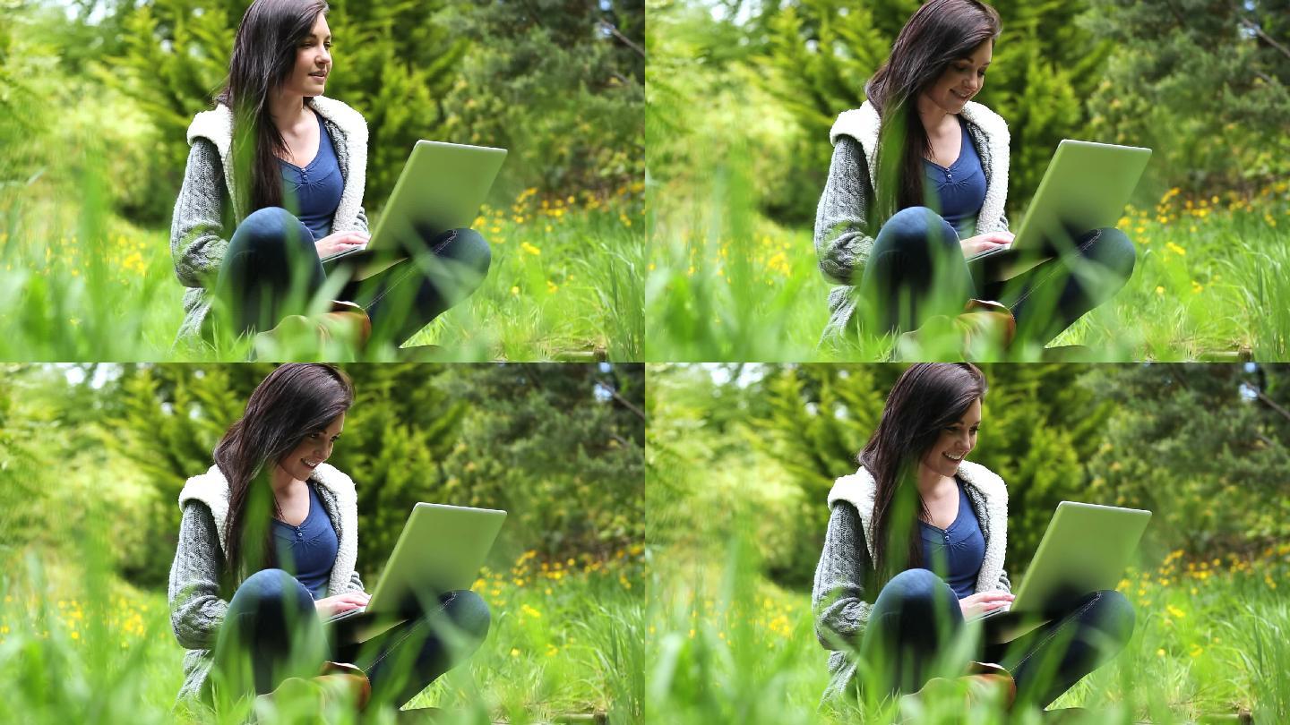 一个坐在草地上用笔记本电脑的漂亮女人