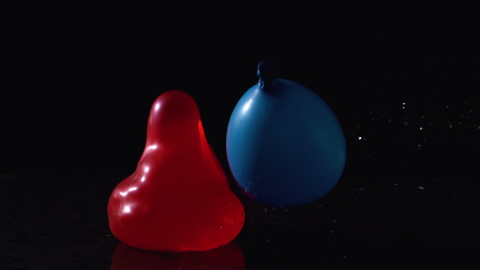 在慢镜头中，红色和蓝色的水球落在黑色背景上