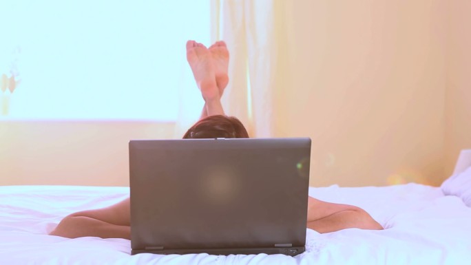 女人躺在卧室的床上看电脑特写
