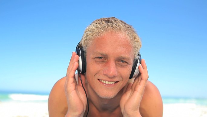 金发男人在海滩上听着音乐