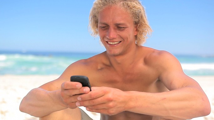 微笑的金发男人在沙滩上用手机
