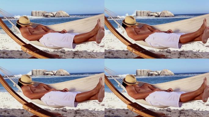 一名戴着草帽的男子躺在沙滩上的吊床上休息