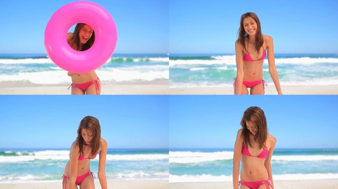 女人穿着粉色比基尼呼啦圈站在沙滩上特写