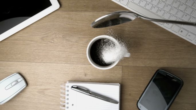 慢镜头里，一茶匙的糖粉洒在了一张办公桌上的一杯咖啡周围