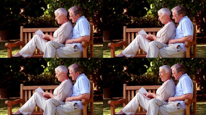 一对老夫妇坐在公园长椅上看书特写