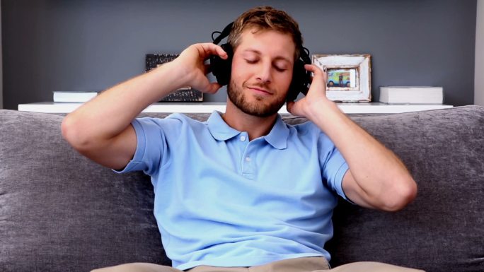 男人听着音乐，坐在家里的沙发上放松