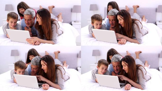 家人躺在床上，拿着笔记本电脑