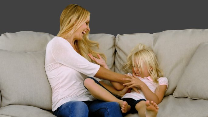 灰色背景下母亲和女儿坐在沙发上玩耍特写