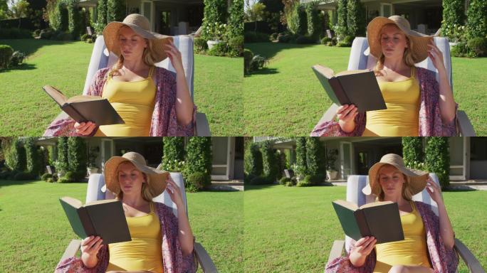 一个白人妇女坐在花园的躺椅上一边看书一边晒日光浴