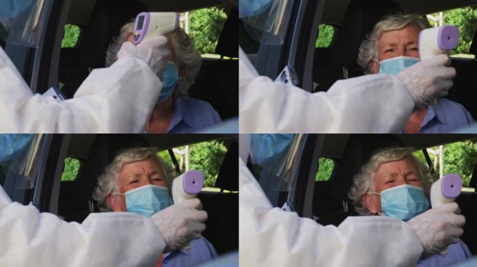 戴着口罩坐在车里，由穿着防护服的人测体温的白人高级妇女