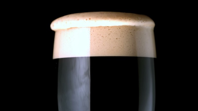 一滴泡沫滴在一杯黑啤酒上特写