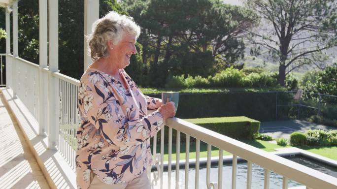 家中阳台上拿着咖啡杯微笑的白人老年女性