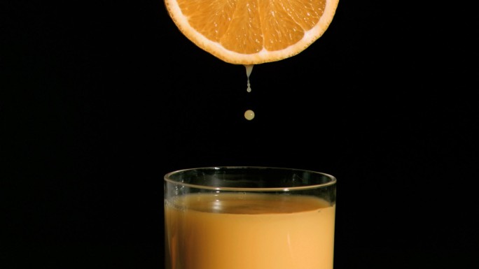 橙汁从橙子中流出落到玻璃杯中特写