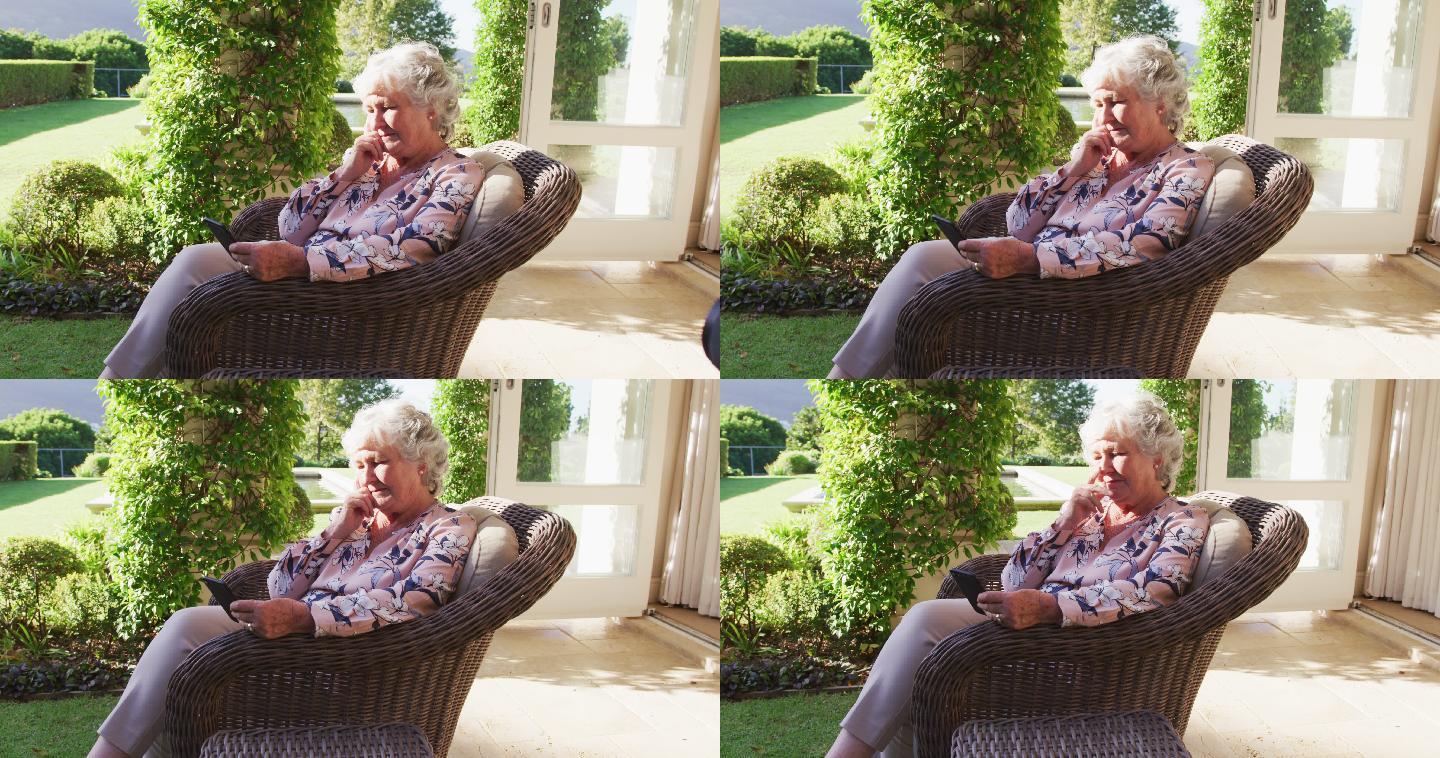 坐在户外椅子上用智能手机思考的白人老年女性