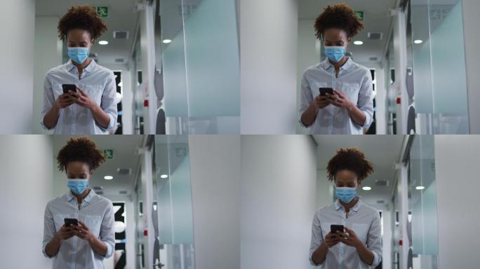一名戴着口罩的混血女商人在办公室走廊上使用智能手机