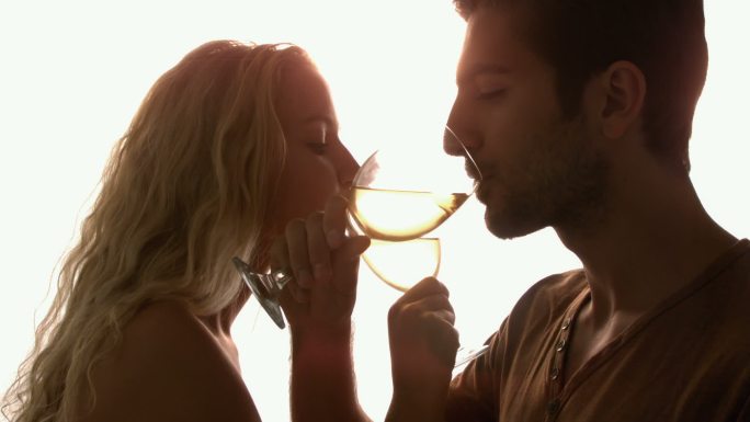 在慢镜头中，一对夫妇在阳光下交叉双臂一起喝酒